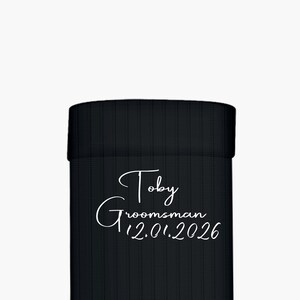 Puede incluir: Enfriador de latas negro con texto blanco "Toby Groomsman 12.01.2026". El texto está en una fuente cursiva. El enfriador de latas está hecho de un material texturizado.