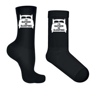 Könnte beinhalten: Zwei schwarze Crew-Socken mit einer weißen Grafik eines Bettes und dem Text "I'd Rather Be Sleeping". Die Socken sind aus einem weichen Material gefertigt und zum Tragen an den Füßen bestimmt.