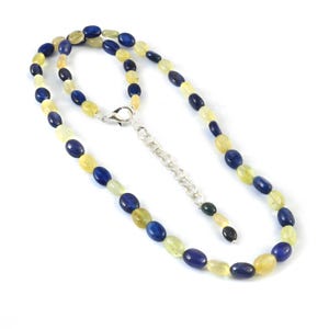 Puede incluir: Un collar hecho de piedras preciosas ovaladas azules y amarillas. El collar tiene un cierre y una cadena de extensión plateados.