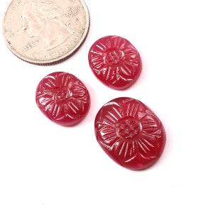 Può includere: Tre pietre preziose ovali di cabochon rosso con un motivo floreale intagliato. Le pietre preziose sono approssimativamente delle dimensioni di una moneta da 25 centesimi di dollaro americano.