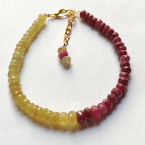 May include: A gemstone bracelet with a colour gradient from yellow to red-purple faceted beads. The bracelet has a gold-coloured clasp and extender chain. The small, round beads create a delicate and elegant piece of jewellery.