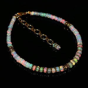 May include: A delicate bracelet featuring small, iridescent opal beads in shades of pink, blue, and green. The beads are strung together with gold-coloured metal accents and a matching chain for adjustable sizing.