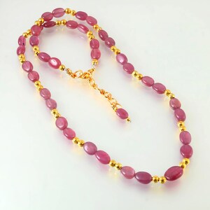 Peut inclure: Un collier composé de pierres précieuses roses ovales alternant avec de petites perles dorées. Le collier est doté d'une chaîne et d'un fermoir dorés. Les pierres précieuses sont polies et le collier est présenté sur une surface blanche.