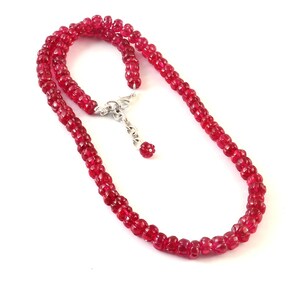 Peut inclure: Un collier de perles rouges avec un fermoir argenté et un petit pendentif en argent.