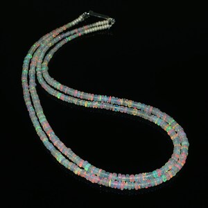 May include: Three strands of iridescent opal necklaces with a delicate pearl strand at the clasp. The opals display a range of colors, including pink, green, and blue, against a white background. The necklaces are displayed on a black surface.
