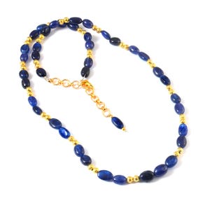 Puede incluir: Un collar con piedras preciosas ovales de color azul oscuro, intercaladas con pequeñas cuentas doradas. El collar tiene una cadena y un cierre dorados. Las piedras preciosas son de un azul intenso y el diseño es elegante.