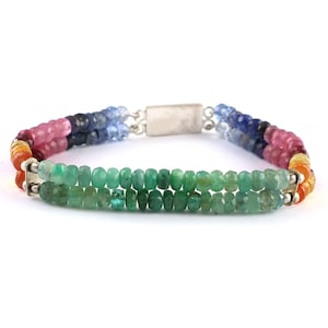 May include: A multi-colored gemstone bracelet with a silver clasp. The bracelet features a rainbow of colors, including orange, yellow, pink, blue, and green. The green gemstones are emerald.
