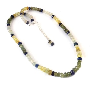 May include: A beaded necklace featuring a variety of gemstones in shades of green, yellow, blue, and clear. The necklace has a silver-colored clasp and extender chain. The gemstones are small and round, strung together to create a delicate piece of jewelry.