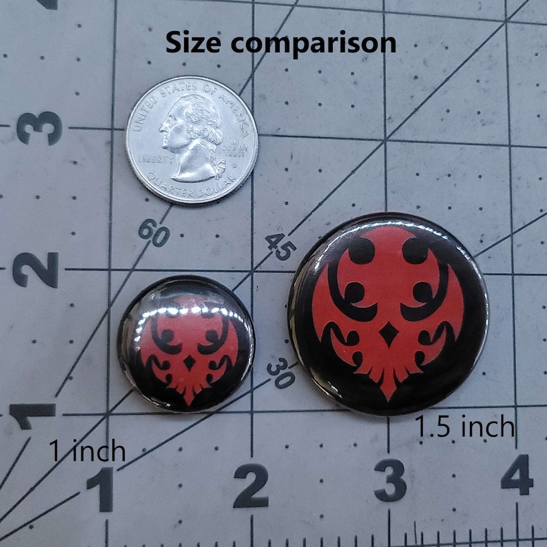 May include: Size comparison of two round buttons with a red and black design. The smaller button is 1 inch in diameter and the larger button is 1.5 inches in diameter.