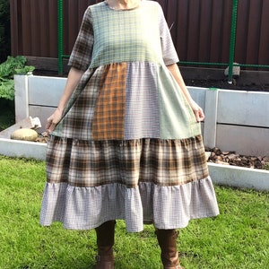May include: A patchwork dress with a tiered skirt. The dress is made of different plaid fabrics in shades of green, brown, orange, and white.