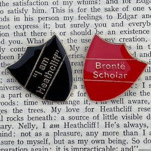 Può includere: Due spille smaltate, una nera con lettere dorate che recitano "I am Heathcliff" e una rossa con lettere dorate che recitano "Brontë Scholar".