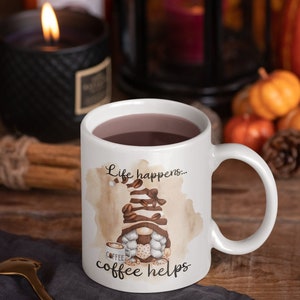 May include: White ceramic coffee mug with a brown and white gnome illustration and the text "Life happens... coffee helps".