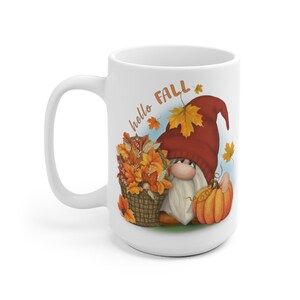 May include: White ceramic coffee mug with a gnome holding a pumpkin and a basket of fall leaves. The mug has the text "hello fall" printed on it.