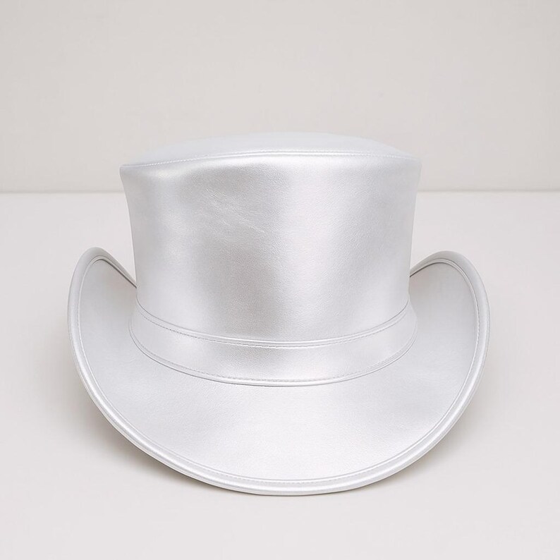May include: A silver top hat with a wide brim and a cylindrical crown. The hat has a shiny, metallic finish and a band around the base of the crown. This formal hat is suitable for special occasions.