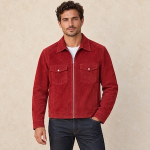 May include: A vibrant red suede jacket featuring a classic collar, a full-length silver-tone metal zip, and two chest pockets with button-down flaps. The jacket is worn over a plain white t-shirt and dark blue denim jeans.