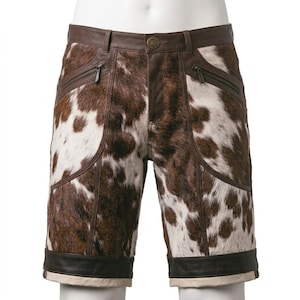 Può includere: Pantaloncini con motivo a pelle di mucca marrone e bianco, caratterizzati da inserti in pelle liscia marrone scuro su vita, tasche e orlo. Il capo presenta due tasche anteriori inclinate con cerniera e una chiusura centrale a bottone.