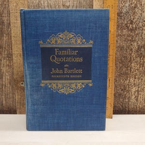May include: A blue hardcover book titled "Familiar Quotations" by John Bartlett, Fourteenth Edition. The title is in gold lettering on a dark blue rectangular label. The book is next to a wooden ruler.