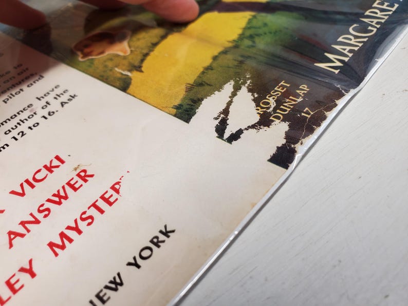 May include: Close-up of a vintage book cover with the title "Vicki Answer Mystery" in red letters. The cover features a colorful illustration and the author's name, Margaret, is visible. The book is slightly damaged.