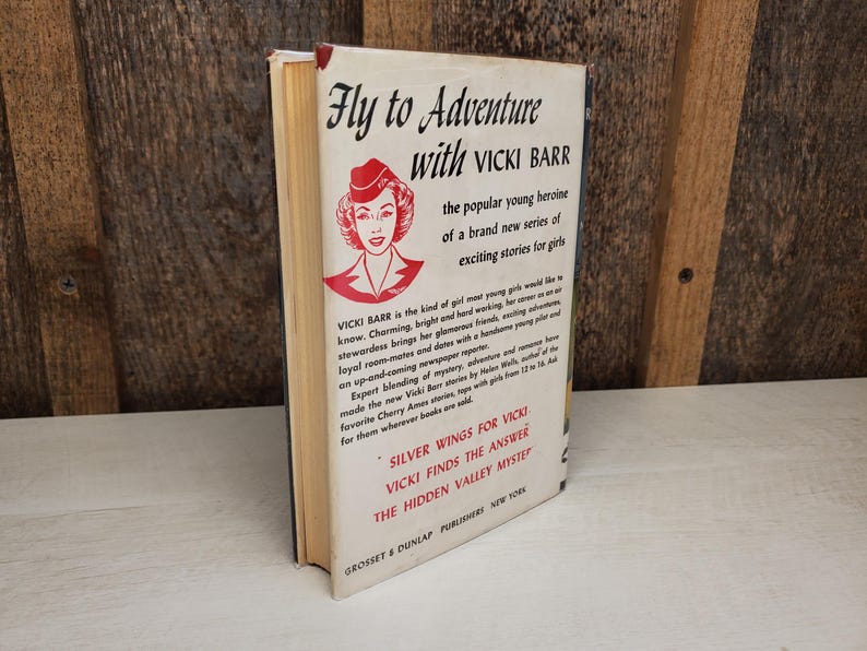 May include: A vintage book titled "Fly to Adventure with Vicki Barr." The cover features a red and white illustration of a woman in a hat. The book is a part of a series of exciting stories for girls.