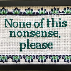 以下が含まれることがあります： 白い背景に緑色の文字で「None of this nonsense, please」と書かれた、額縁に入ったクロスステッチ。文字は緑と青の花の縁取りで囲まれています。