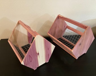 May include: Two wooden storage baskets with a handle. The baskets are made of cedar wood with a natural reddish-brown color and a wire mesh interior. The baskets are angled and have a handle for carrying.