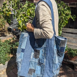 以下が含まれることがあります： パッチワークデザインの大きなデニムトートバッグ。バッグは、明るいパッチと暗いパッチが混ざった、さまざまなブルーデニムの色合いで作られています。バッグは幅広のショルダーストラップと長方形の形をしています。