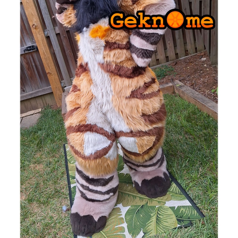 May include: A brown and white striped furry costume with black paws and a black tail. The costume is standing on a green and white patterned rug. The text "Geknome" is visible in the image.
