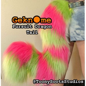 May include: A colourful fursuit dragon tail, featuring hot pink and lime green fur. The tail is long and curved, with a fluffy texture. The image includes the text "Geknome Fursuit Dragon Tail" and the seller's social media handle.