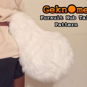 May include: White faux fur nub tail for a fursuit. The tail is attached to a person's waist with a brown belt. The text "Geknome Fursuit Nub Tail Pattern" is visible in the image.