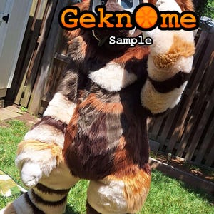 May include: A full-body fursuit in shades of brown, white, and tan, with a furry texture. The suit has a head and paws, and the text "Geknome Sample" is visible on the head. The fursuit is standing on green grass.