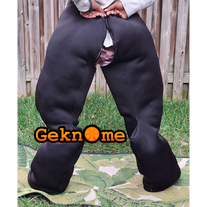 May include: Black pants with a zipper down the center back seam. The pants are made of a thick, stretchy material and have a slight sheen. The pants are pulled down to reveal a patterned underwear.