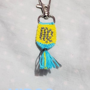 May include: A yellow and blue keychain with a gray Virgo zodiac symbol and a blue tassel.