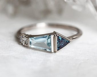 May include: A silver ring with a light blue aquamarine gemstone and a dark blue triangular gemstone. The ring has a delicate design with small diamonds on the band.