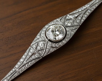 Op de afbeelding: Een zilveren armband met een grote, ronde, heldere diamant in het midden, omringd door kleinere diamanten. De armband heeft een Art Deco-ontwerp met geometrische patronen en ligt op een donkerhouten oppervlak.