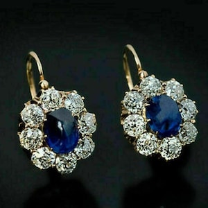 May include: A pair of gold earrings with a blue sapphire gemstone surrounded by smaller diamonds. The earrings have a floral design and dangle from a hook.