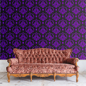 May include: A vintage-style couch with a tufted back and arms, upholstered in a rich brown fabric. The couch is positioned in front of a black and purple damask wallpaper with a skull pattern.