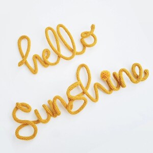 May include: Yellow knitted yarn letters spelling out "hello sunshine" with a small yellow pom pom on the "s" in sunshine.