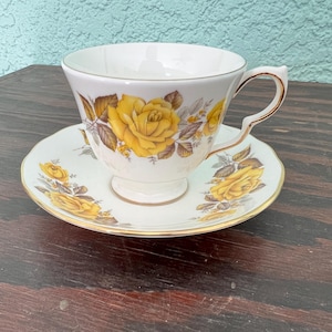 Könnte beinhalten: Weißes Tee-Service mit gelbem Rosenmuster. Die Tasse und Untertasse sind mit gelben Rosen und goldenen Rändern verziert. Ein elegantes Set für den Nachmittagstee.