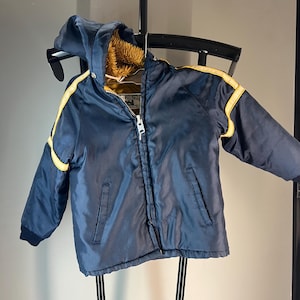 May include: Navy blue children's jacket with a hood and yellow stripes on the sleeves. The jacket has a zipper closure and two front pockets. The interior lining is a light brown faux fur.