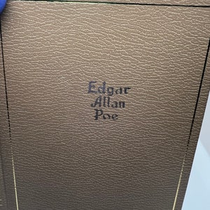 May include: A brown leather-bound book with gold edging. The title "Edgar Allan Poe" is embossed in black on the front cover.