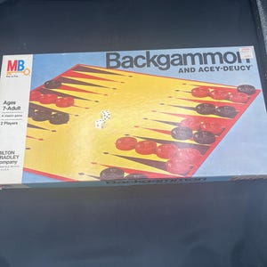 May include: A vintage Backgammon and Acey-Deucy board game box. The box features a yellow playing surface with red and black triangles, and red and black game pieces. The dice are visible on the board. The box reads "Backgammon" and "Ages 7-Adult".