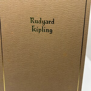 May include: A brown leather-bound book with gold edging. The title "Rudyard Kipling" is embossed in green on the front cover.