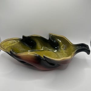 May include: A ceramic bowl shaped like a leaf with a green, black, and red glaze. The bowl has a unique, organic shape and is perfect for serving snacks or fruit.