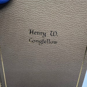 May include: A brown leather-bound book with gold accents and the text "Henry W. Longfellow" embossed on the front cover.