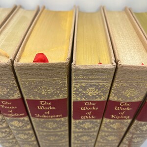 May include: A set of six hardcover books with gold-colored spines and red labels. The titles on the labels are "The Poems of Longfellow", "The Works of Shakespeare", "The Works of Wilde", and "The Works of Kipling".