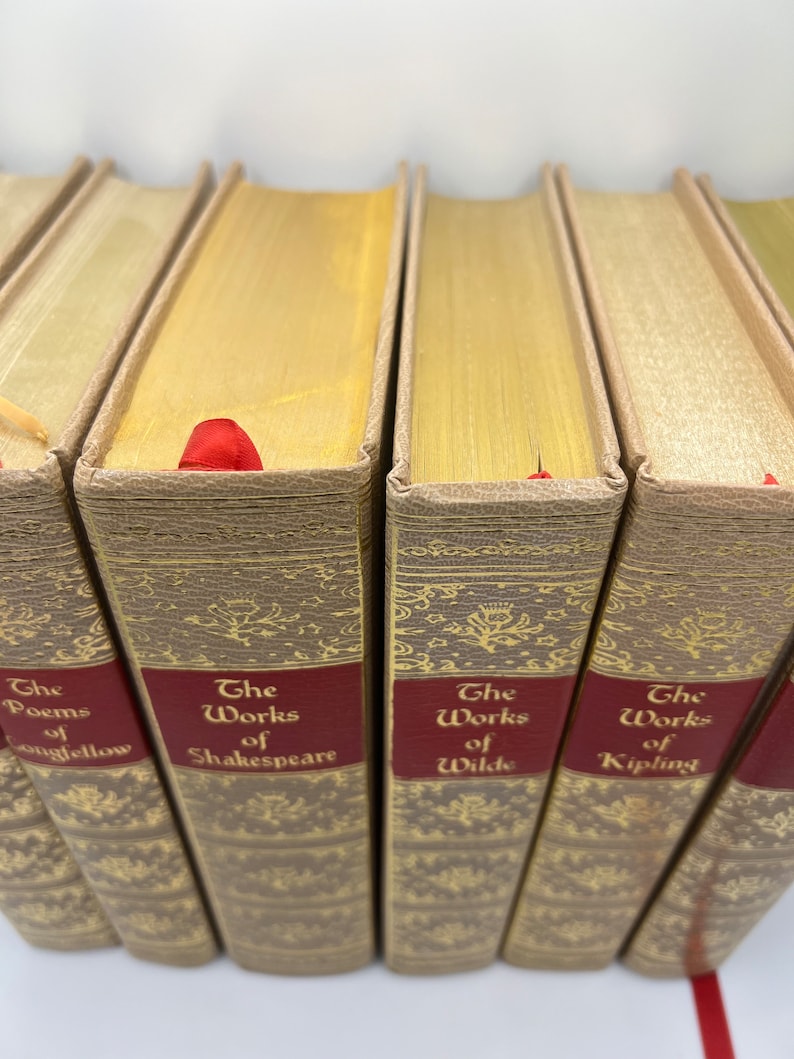 May include: A set of six hardcover books with gold-colored spines and red labels. The titles on the labels are "The Poems of Longfellow", "The Works of Shakespeare", "The Works of Wilde", and "The Works of Kipling".