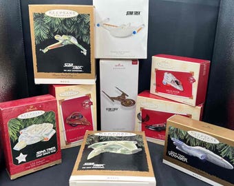May include: A collection of eight Hallmark Keepsake Star Trek ornaments in their original rectangular cardboard boxes. The boxes feature various Star Trek starship illustrations, including the USS Defiant, Bird of Prey, and Voyager, with the Hallmark logo.