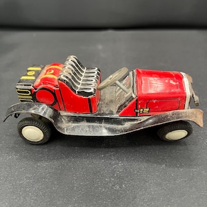 May include: A vintage toy car in red and black. The car features a detailed design with a red body, black seats, and white tires. The steering wheel and other details are visible. This collectible toy car is a classic.