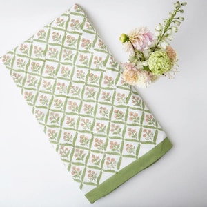 May include: A white cotton tablecloth with a green and pink floral pattern. The tablecloth has a green border and is folded in half.