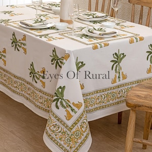 Puede incluir: Un mantel blanco con un estampado repetido de hojas de plátano verdes y estampado de leopardo amarillo. La mesa está puesta con manteles individuales, servilletas y platos a juego. El texto "Eyes Of Rural" es visible.